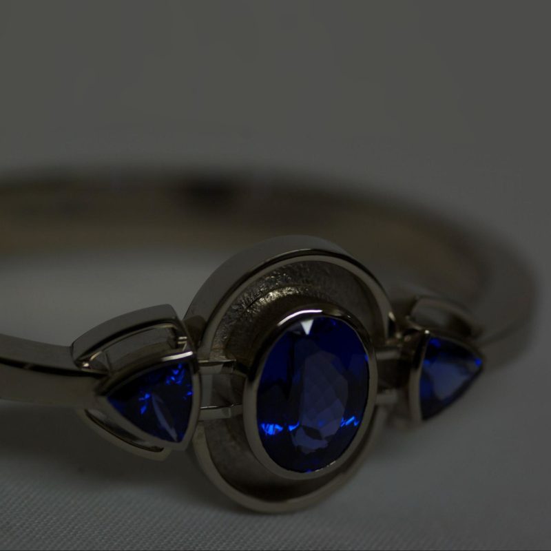 Rudolf Heltzel white gold engagement ring bezel set with 1 round and 2 trilliant cut sapphires